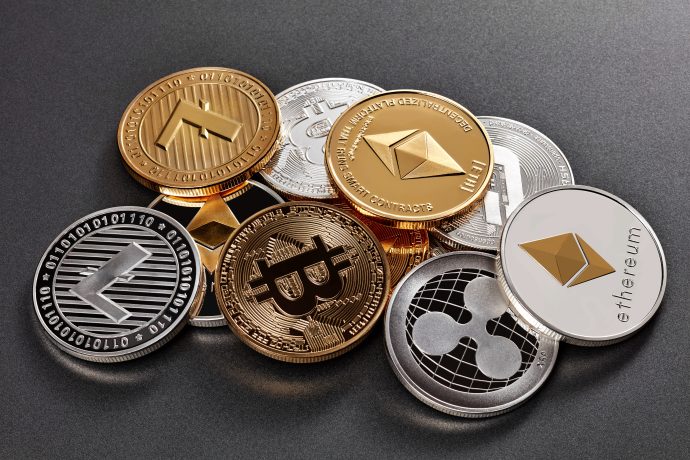 Ein Stapel verschiedener physischer Kryptowährungsmünzen, darunter Bitcoin, Ethereum, Litecoin und Ripple, angeordnet auf einer dunklen Oberfläche. Die herausragende Bitcoin-Münze sticht aus dieser beeindruckenden Sammlung hervor.