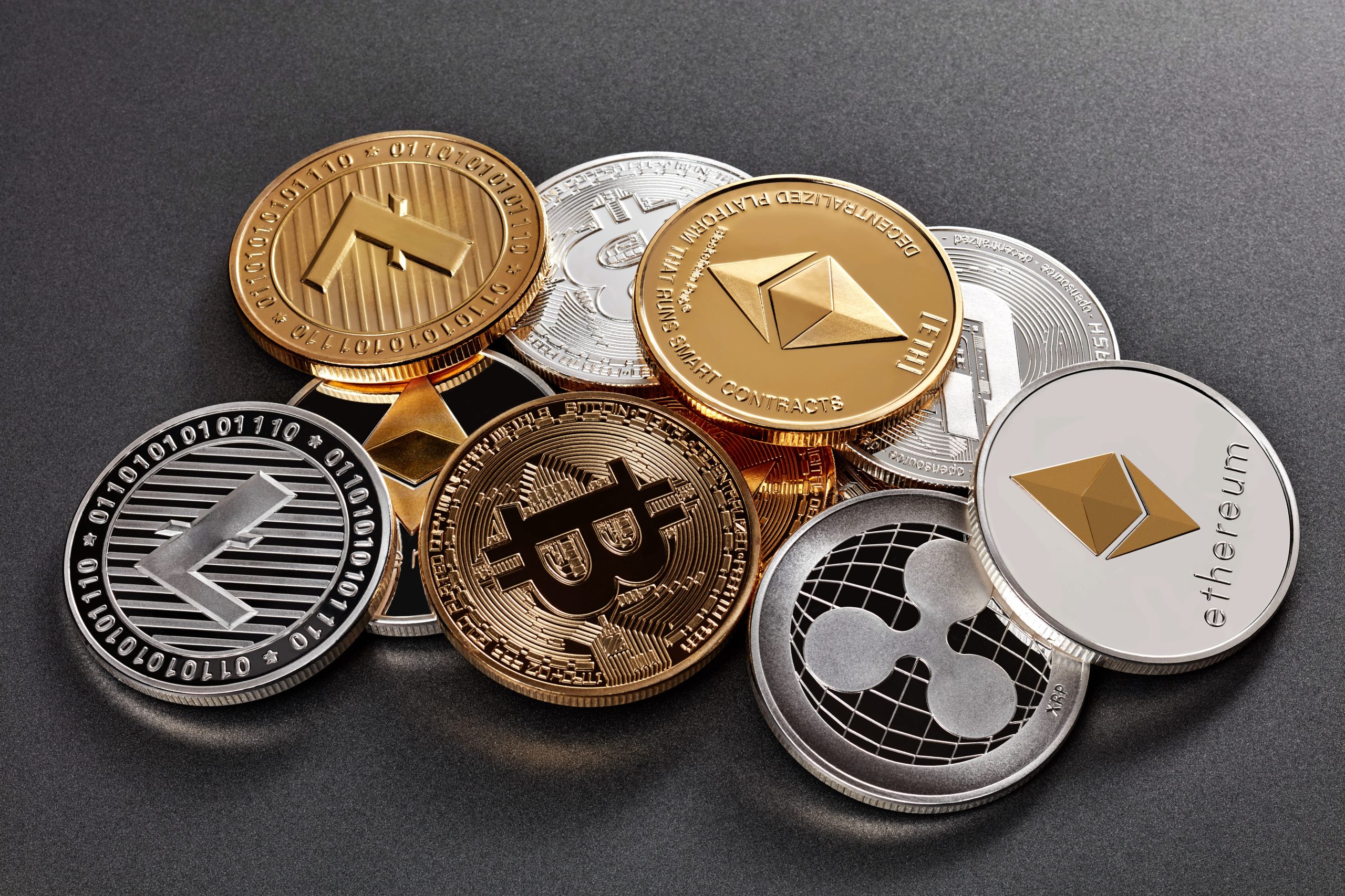 Ein Stapel verschiedener physischer Kryptowährungsmünzen, darunter Bitcoin, Ethereum, Litecoin und Ripple, angeordnet auf einer dunklen Oberfläche. Die herausragende Bitcoin-Münze sticht aus dieser beeindruckenden Sammlung hervor.