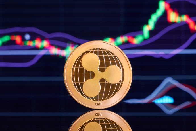Eine goldene XRP-Münze steht vor einem digitalen Bildschirm, der bunte Kryptowährungspreisdiagramme und -grafiken anzeigt.