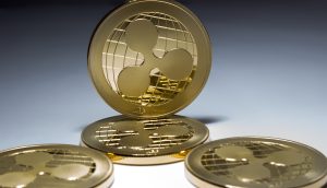 Vier goldfarbene XRP-Münzen werden angezeigt, wobei eine XRP-Münze aufrecht steht und drei flach auf einer geneigten Fläche liegen.