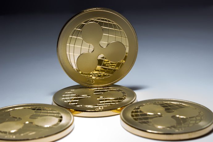 Vier goldfarbene XRP-Münzen werden angezeigt, wobei eine XRP-Münze aufrecht steht und drei flach auf einer geneigten Fläche liegen.