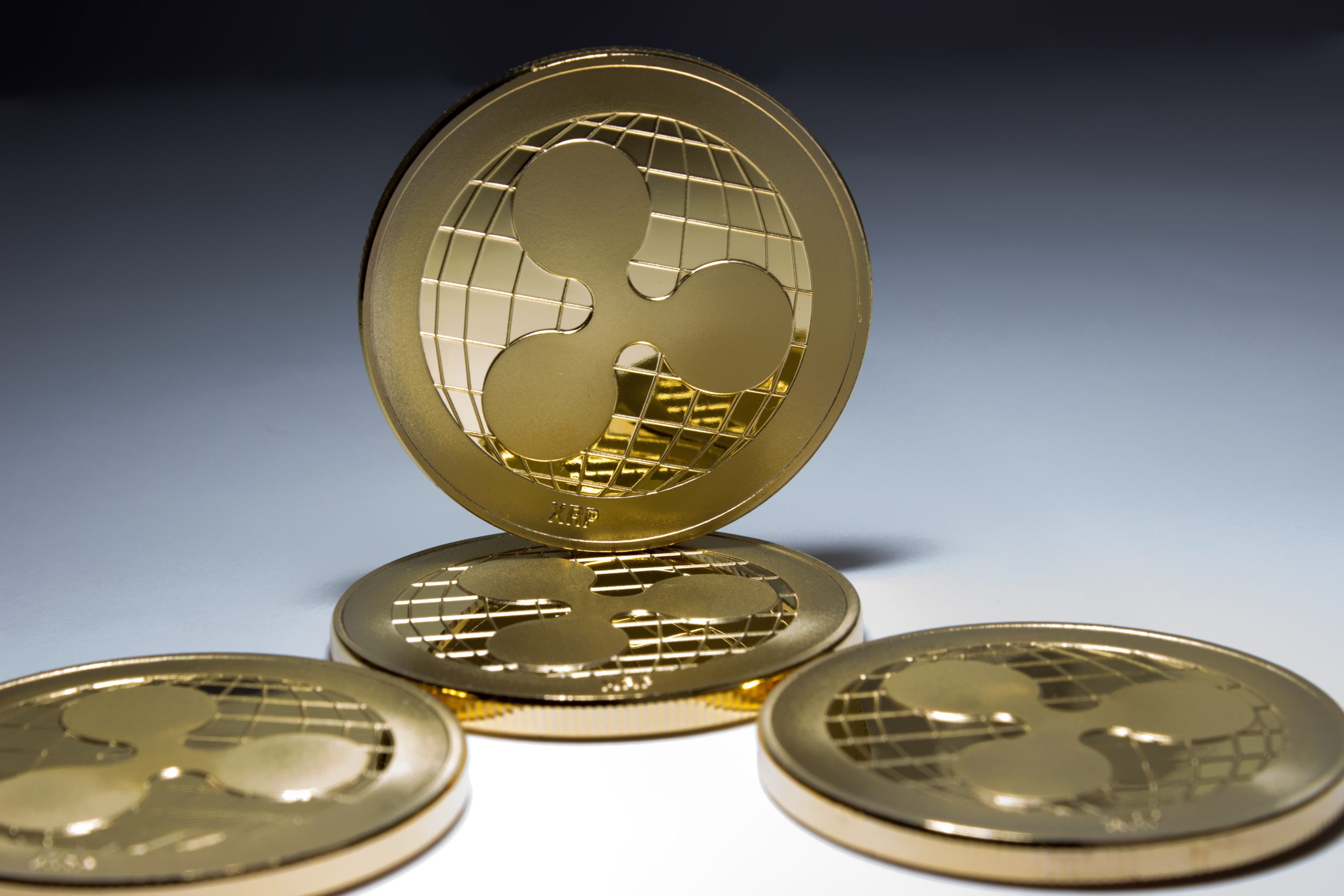 Vier goldfarbene XRP-Münzen werden angezeigt, wobei eine XRP-Münze aufrecht steht und drei flach auf einer geneigten Fläche liegen.