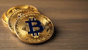 Drei physische Bitcoin-Token mit einer goldenen Farbe und dem ikonischen blauen Symbol sind auf einer hölzernen Oberfläche platziert und symbolisieren den Wert und die Sicherheit einer Bitcoin-Treasury.