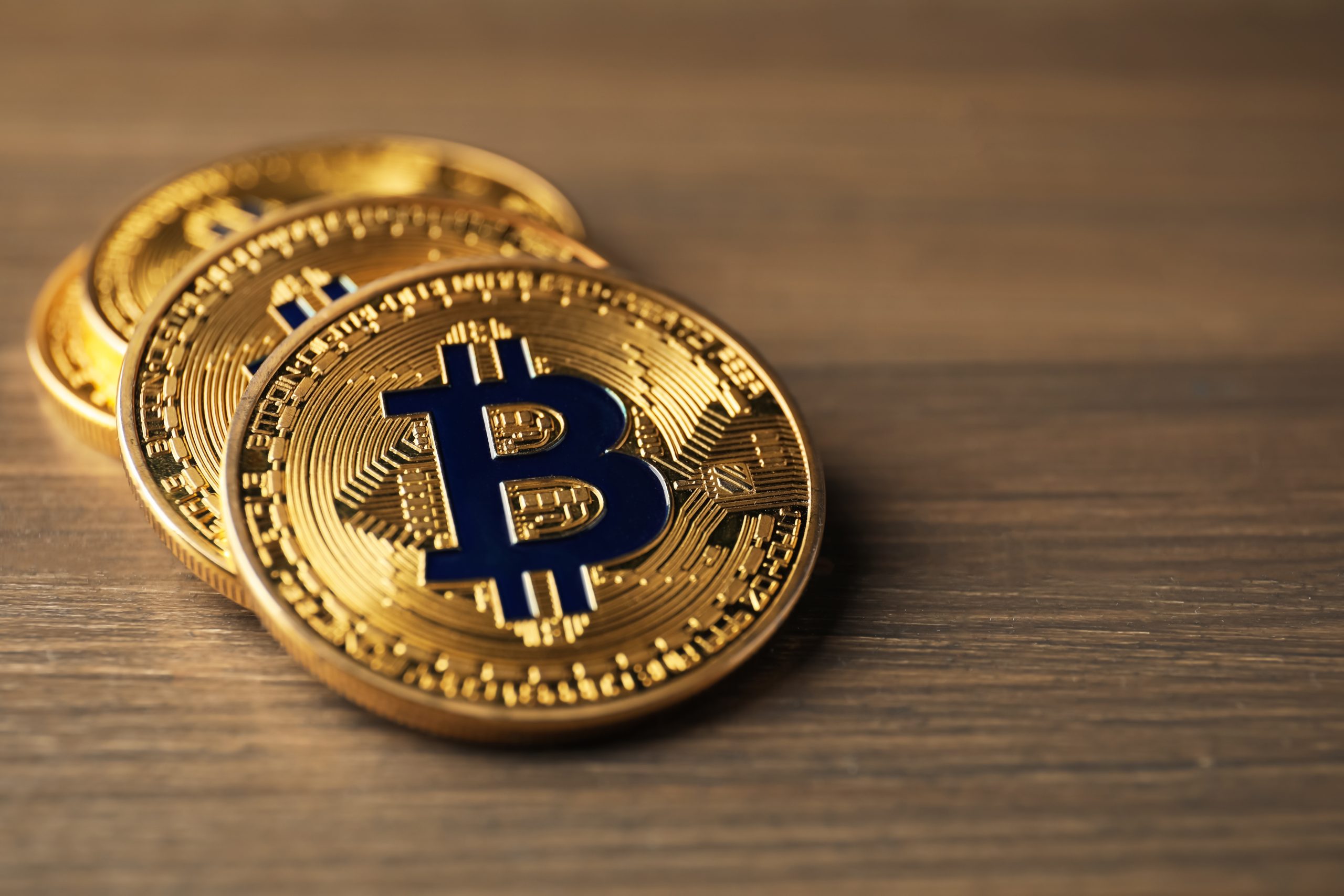 Drei physische Bitcoin-Token mit einer goldenen Farbe und dem ikonischen blauen Symbol sind auf einer hölzernen Oberfläche platziert und symbolisieren den Wert und die Sicherheit einer Bitcoin-Treasury.