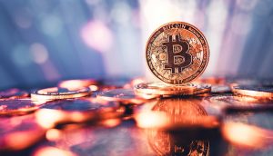 Eine physische Darstellung eines Bitcoins steht aufrecht zwischen verstreuten Münzen, mit einem verschwommenen, bunten Hintergrund und Reflexionen auf der Oberfläche - ein Symbol für die Trends, die in jeder aktuellen Bitcoin-Prognose zu sehen sind.