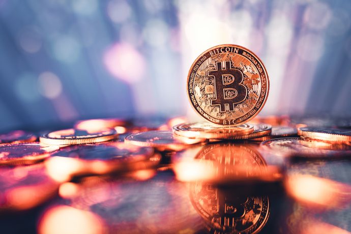 Eine physische Darstellung eines Bitcoins steht aufrecht zwischen verstreuten Münzen, mit einem verschwommenen, bunten Hintergrund und Reflexionen auf der Oberfläche - ein Symbol für die Trends, die in jeder aktuellen Bitcoin-Prognose zu sehen sind.