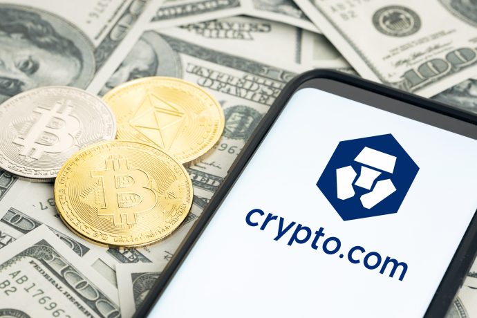 Drei Kryptowährungsmünzen und ein Smartphone mit dem Crypto.com-Logo sind auf mehreren US-Dollarnoten platziert, um die Verbindung zwischen digitalen Vermögenswerten und traditionellen Finanzen zu verdeutlichen, die Crypto.com herstellt.