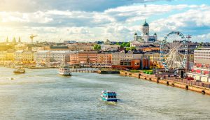 Blick auf die Hafenpromenade von Helsinki mit Booten auf dem Wasser, bunten Gebäuden, einem Riesenrad und dem Dom von Helsinki im Hintergrund bei teilweise bewölktem Himmel - Heimat innovativer Unternehmen wie Tesseract und der lebendigen DeFi-Portfoliomanager-Szene der FIN-FSA.