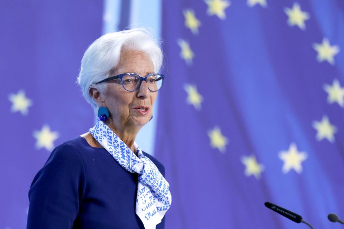 Eine ältere Frau mit weißem Haar, Brille und Kopftuch spricht an einem Podium mit der Aufschrift "EZB" vor einem Hintergrund mit gelben Sternen auf blauem Grund.