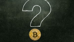 Eine goldene Bitcoin-Münze befindet sich unter einem großen Fragezeichen, das mit weißer Kreide auf eine dunkelgrüne Tafel gezeichnet wurde und Fragen und Neugierde rund um Bitcoin symbolisiert.