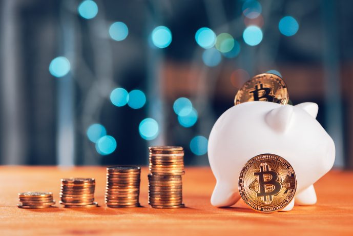 Ein weißes Sparschwein mit Bitcoin-Münzen und mehreren Stapeln von Münzen auf einer hölzernen Oberfläche symbolisiert das Sparen für die Zukunft, mit blauen Bokeh-Lichtern im Hintergrund - perfekt für die Illustration von Bitcoin-Rente-Konzepten.
