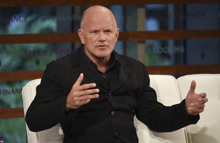 Mike Novogratz in einem schwarzen Anzug sitzt auf einer weißen Couch und gestikuliert mit den Händen, während er in einem Interview oder einer Podiumsdiskussion über Solana spricht.