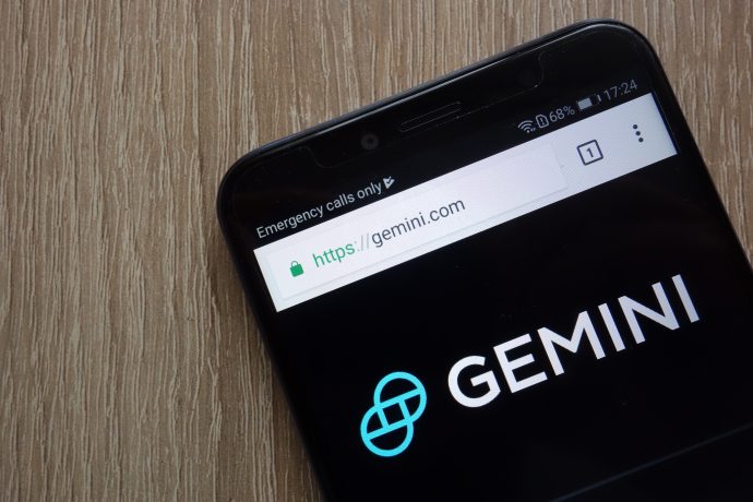 Ein Smartphone zeigt die Website der Kryptowährung Gemini an, wobei die URL im Browser sichtbar ist und das unverwechselbare Gemini-Logo prominent auf dem Bildschirm angezeigt wird.