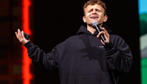 Jack Mallers gilt als Perma-Bulle Jack Mallers, die einen schwarzen Kapuzenpulli trägt, hält ein Mikrofon und ein Telefon in der Hand, während sie auf der Bühne spricht oder singt und möglicherweise darüber diskutiert, wie der Bitcoin-Kurs steigen könnte, oder die Erkenntnisse von Jack Mallers erwähnt.