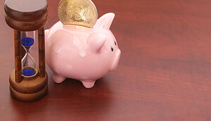 Ein Sparschwein mit einer Bitcoin-Münze darin sitzt neben einer kleinen Sanduhr auf einer hölzernen Oberfläche und symbolisiert das Konzept der Bitcoin-Rente und des Sparens für die Zukunft.