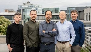 Fünf Männer, die nebeneinander auf einem Dach in München stehen, mit modernen Bürogebäuden im Hintergrund unter einem wolkenverhangenen Himmel - ein Spiegelbild ihres gemeinsamen Wachstumskurses im Bereich Krypto-Verwahrung.