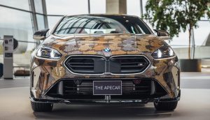 Ein BMW mit einer Schlangenhautverkleidung in Tarnfarben ist im Innenraum ausgestellt und auf einer Frontplatte mit THE APECAR beschriftet - ein Blickfang für jeden Auto- oder NFT-Liebhaber.