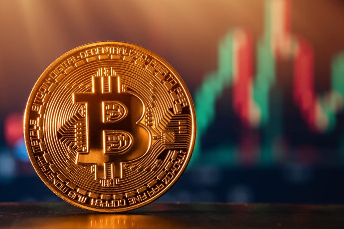 Eine physische Bitcoin-Münze wird vor einem unscharfen Hintergrund von Finanzmarktcharts und Kerzenleuchtern gezeigt und symbolisiert den wachsenden Einfluss von Bitcoin-ETFs im modernen Handel.