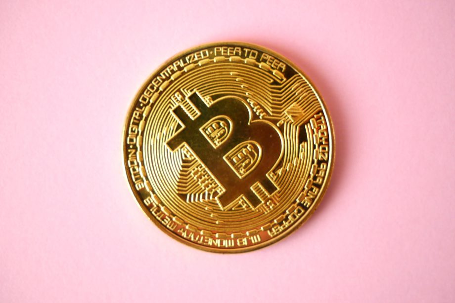 Eine goldfarbene physische Bitcoin-Münze mit dem Bitcoin-Symbol wird auf einem rosafarbenen Hintergrund dargestellt und spiegelt die Meinung eines Analysten zur Wahrscheinlichkeit eines neuen Bitcoin-Allzeithochs wider.