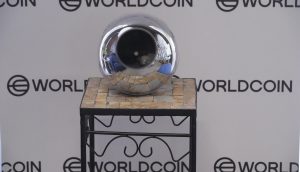 Ein Irisscanner von Worldcoin steht vor einem Hintergrund mit wiederholten Worldcoin-Logos.
