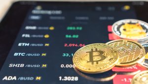 Nahaufnahme von physischen Bitcoin-Münzen auf einem digitalen Bildschirm, auf dem Kryptowährungskurse und Handelspaare angezeigt werden, darunter auch Trendwerte wie Ethena.