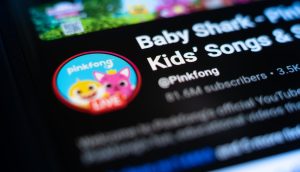 Nahaufnahme der Pinkfong-YouTube-Kanalseite auf einem Bildschirm mit dem Profilbild, dem Kanalnamen, der Abonnentenzahl und einer Erwähnung von Baby Shark Token in den Videobeschreibungen.