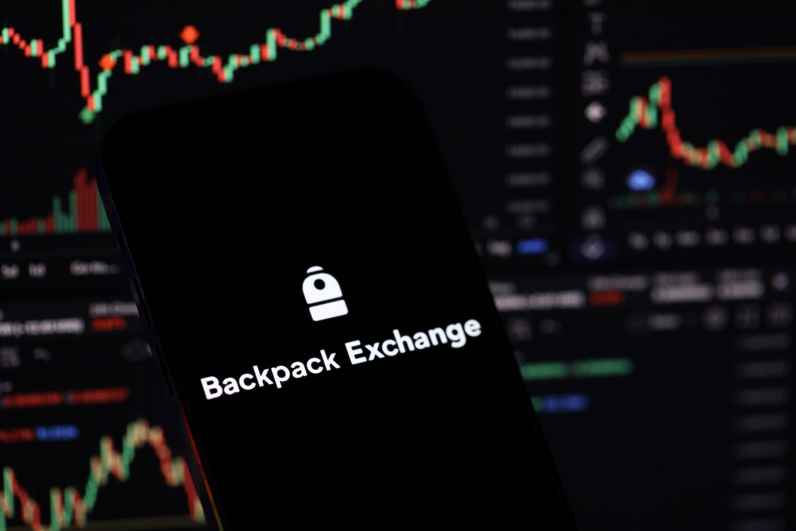 Auf einem Smartphone-Bildschirm werden das Logo und der Name der Backpack Exchange angezeigt. Im Hintergrund sind unscharfe Charts für den Handel mit Kryptowährungen und der Perpetuals-Handel zu sehen, was die Präsenz der Börse als führende KryptoBörse in Europa unterstreicht.
