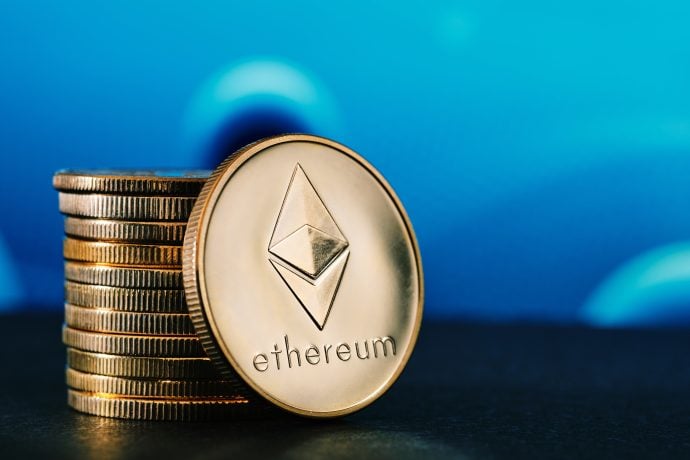 Ein Stapel goldfarbener Münzen, eine davon mit dem Ethereum-Logo und dem Wort "Ethereum" davor, hebt sich von einem blauen Hintergrund ab.