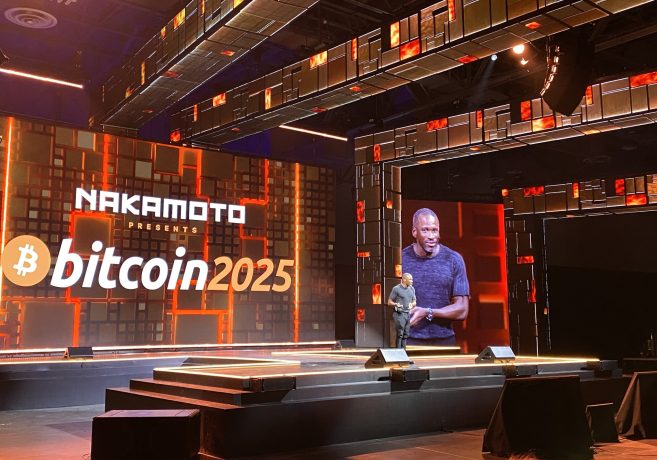 Ein Redner steht auf der Bühne einer Bitcoin 2025-Veranstaltung, während im Hintergrund auf großen Bildschirmen NAKAMOTO PRESENTS bitcoin 2025 zu sehen ist - Arthur Hayes und andere führende Bitcoin-Experten werden ihre Visionen für die Zukunft vorstellen.