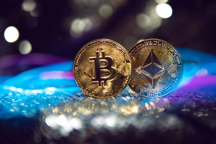Zwei physische Münzen mit dem Bitcoin- und dem Ethereum-Logo werden nebeneinander auf einer spiegelnden Oberfläche angezeigt, wobei verschwommene Lichter im Hintergrund elegant leuchten.