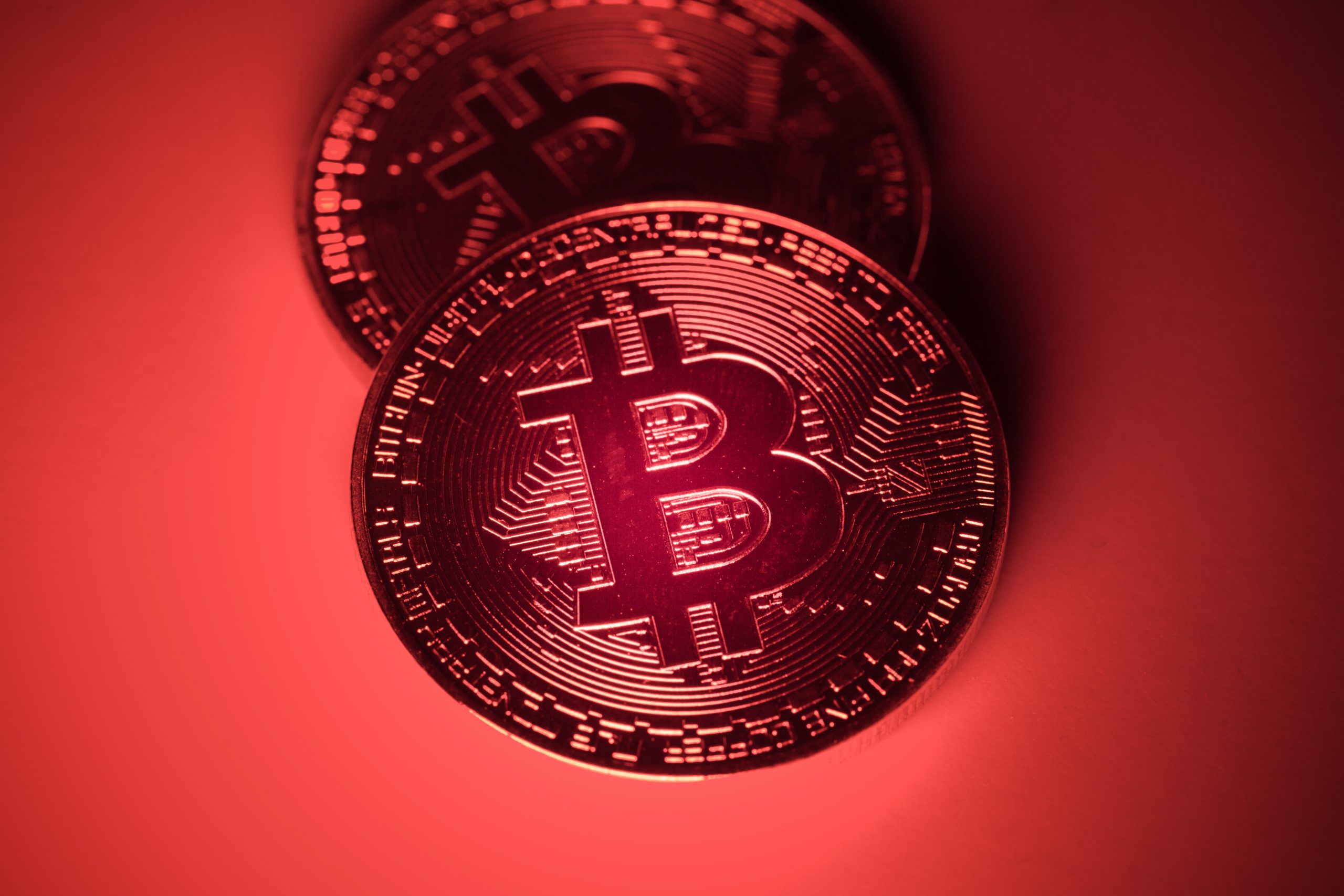 Zwei physische Bitcoin-Token (BTC) werden unter rotem Licht gezeigt, wobei auf ihrer Oberfläche kreislaufähnliche Muster zu erkennen sind, die das digitale Wesen von Bitcoin hervorheben.