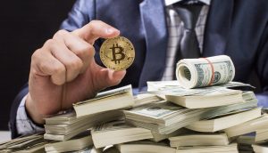 Eine Person im Anzug hält einen Bitcoin-Token über einem großen Stapel von US-Dollar-Scheinen, auf dem eine Rolle Bargeld liegt, was den Kontrast zwischen Kryptowährung und herkömmlicher Währung verdeutlicht.