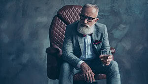 Ein älterer Mann mit weißem Bart und Brille sitzt in einem braunen Ledersessel, trägt einen grau karierten Anzug, hält ein Glas Whiskey in der Hand und denkt über seine Bitcoin-Investitionen nach.