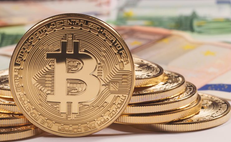 Ein Stapel goldfarbener Bitcoin-Token wird vor unscharfen Euro-Banknoten gezeigt, um die Attraktivität von Krypto-Vermögenswerten und Überlegungen wie Jahreshaltefrist für Anleger zu unterstreichen.