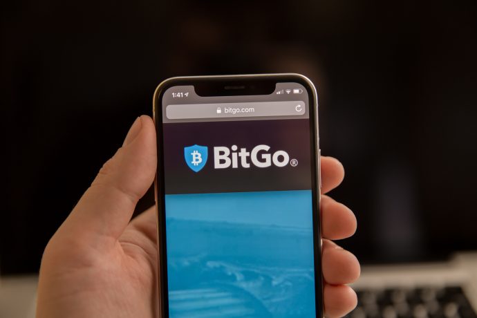 Eine Hand hält ein Smartphone, auf dessen Bildschirm die BitGo-Website angezeigt wird, wobei das BitGo-Logo deutlich oben zu sehen ist.
