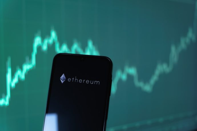 Ein Smartphone mit dem Ethereum-Logo wird vor einem unscharfen digitalen Diagramm mit einer steigenden Ethereum-Trendlinie gezeigt.