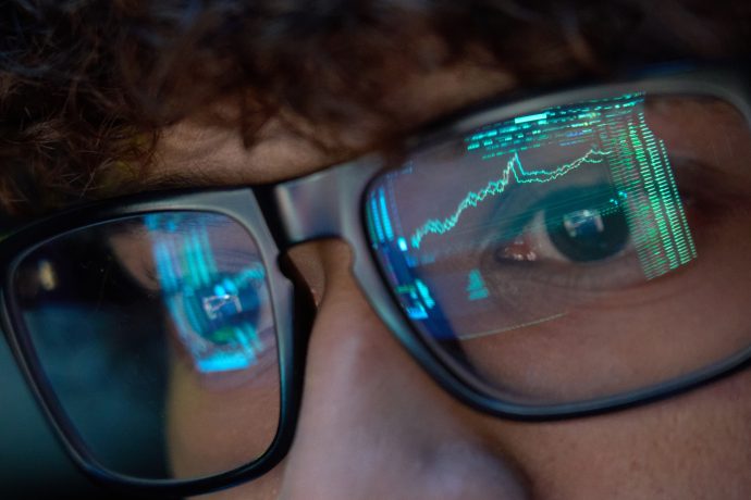 Nahaufnahme einer Person, die eine Brille mit Hyperliquid-Computerbildschirmreflexionen trägt, auf denen Liniendiagramme und Datendiagramme zu sehen sind.