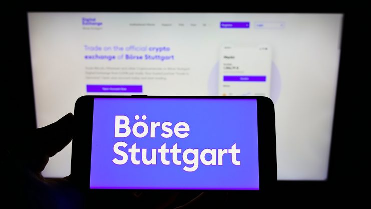 Ein Smartphone zeigt den Schriftzug Börse Stuttgart vor einem unscharfen Computerbildschirm, der die Website der Kryptobörse Börse Stuttgart zeigt und den Fokus der Plattform auf Tokenisierung und innovative digitale Assets hervorhebt.
