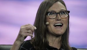 Eine Frau mit Brille und Headset-Mikrofon spricht während einer Veranstaltung angeregt über Solana, während der Hintergrund in Lila und Blau verschwimmt.