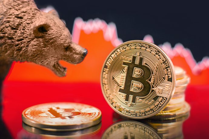 Eine Bärenfigur steht neben Bitcoin-Münzen mit einer abwärts gerichteten roten Grafik im Hintergrund, die einen bärischen Bitcoin-Kurs und einen rückläufigen Kryptowährungsmarkt symbolisiert.