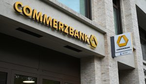 Das Äußere einer Commerzbank-Filiale mit gelber Beschilderung und Logo auf einem modernen Backsteingebäude, das auf mögliche Krypto-Dienste im Inneren hinweist.