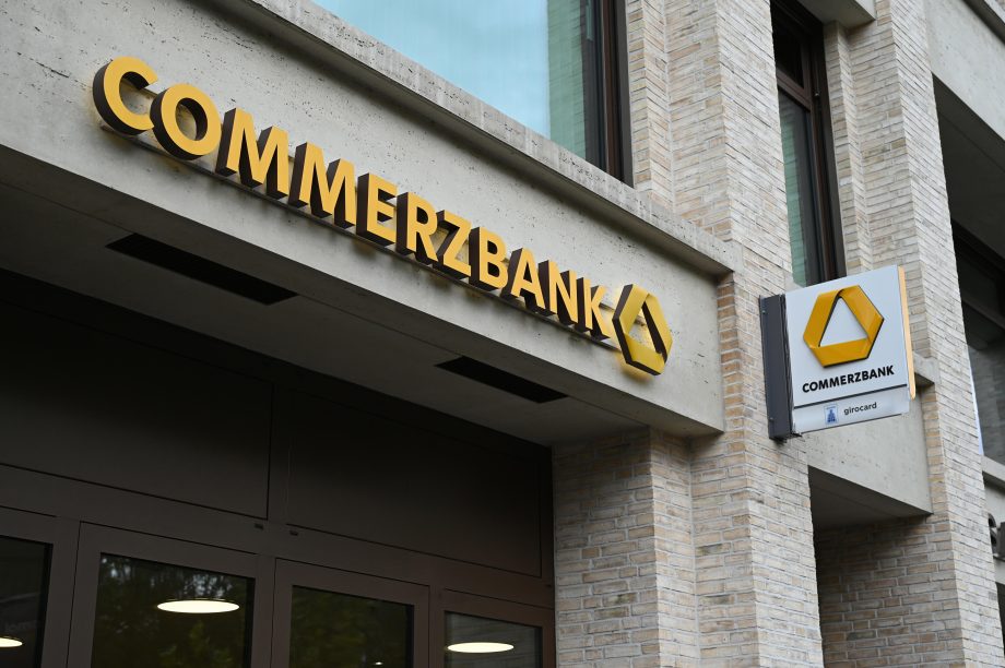 Das Äußere einer Commerzbank-Filiale mit gelber Beschilderung und Logo auf einem modernen Backsteingebäude, das auf mögliche Krypto-Dienste im Inneren hinweist.