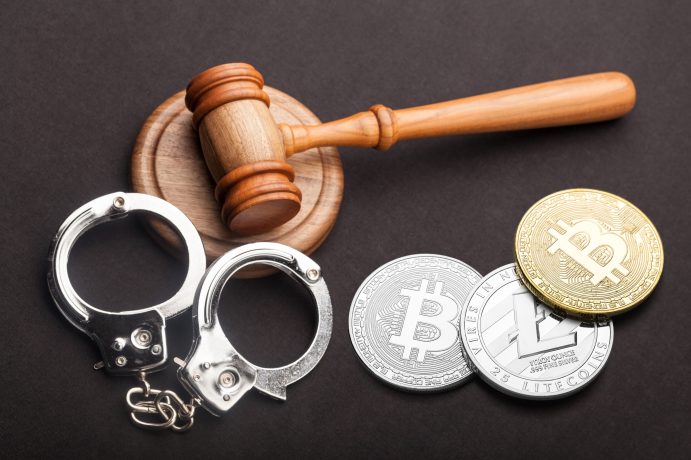 Ein Richterhammer, ein Paar Handschellen und drei Kryptowährungsmünzen sind auf einer dunklen Fläche angeordnet und symbolisieren die Krypto-Kriminalität und die Auswirkungen der jüngsten Mega-Razzia auf Bankkonten.
