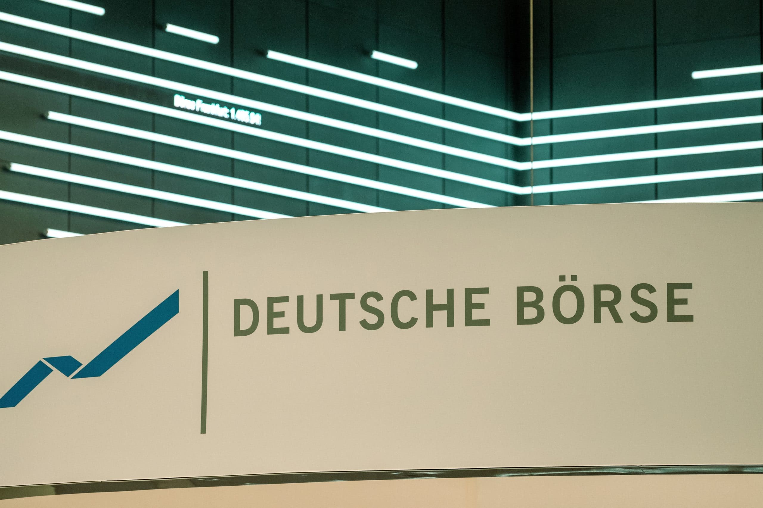 Ein Schild mit dem Logo und dem Namen der Deutschen Börse vor einer modernen, beleuchteten Wand mit horizontalen Lichtbändern unterstreicht den Fokus auf Innovation und Integration, einschließlich der Entwicklungen bei Stablecoins.