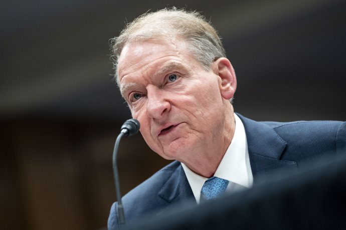Ein Mann mittleren Alters im Anzug spricht bei einer scheinbar formellen Veranstaltung oder Anhörung in ein Mikrofon und spricht über Themen wie Krypto und die Zeit, die dafür gekommen ist.