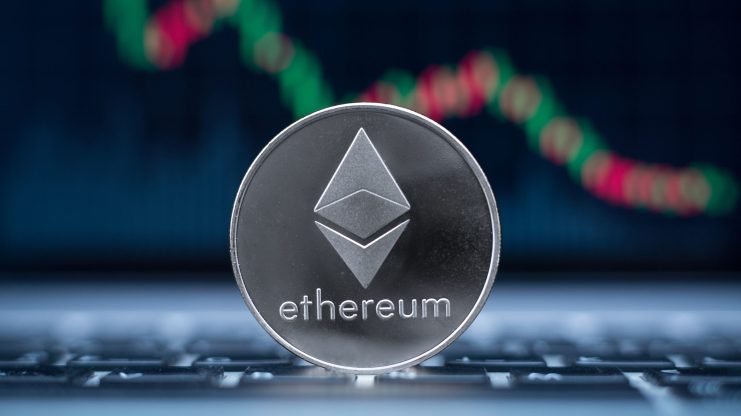 Eine silberne Ethereum-Münze steht auf einer Laptop-Tastatur mit einem verschwommenen roten und grünen Candlestick-Chart im Hintergrund und symbolisiert die Ethereum-Reserven an Börsen auf ihrem niedrigsten Stand.