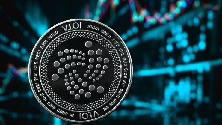 Eine physische IOTA-Kryptowährungsmünze wird vor einem unscharfen digitalen Finanzdiagramm mit bunten Grafiklinien gezeigt, das die dynamische Welt des IOTA-Handels hervorhebt.
