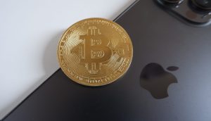 Eine goldene Bitcoin-Münze liegt auf der Rückseite eines schwarzen iPhone 17, auf dem das Apple-Logo zu sehen ist.