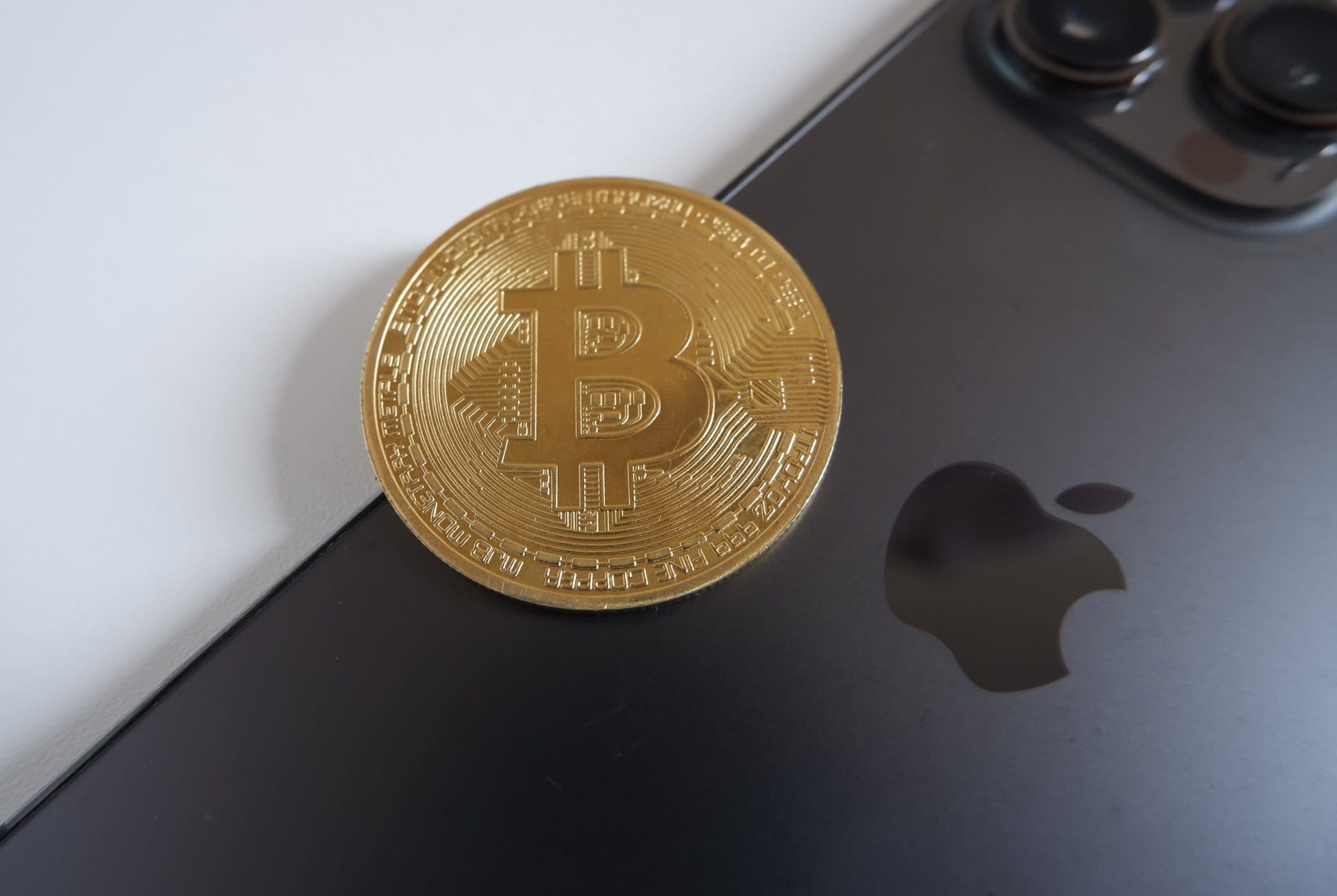 Eine goldene Bitcoin-Münze liegt auf der Rückseite eines schwarzen iPhone 17, auf dem das Apple-Logo zu sehen ist.