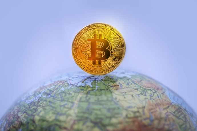 Eine goldene Bitcoin-Münze, die auf einer Weltkugel balanciert, symbolisiert die globale Präsenz von Krypto und Kryptowährung.